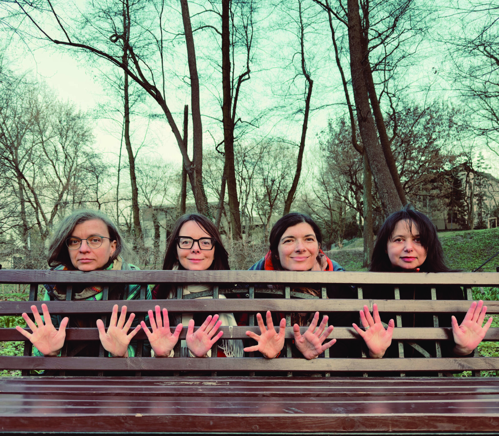 four people showing their hands from between a wooden bench