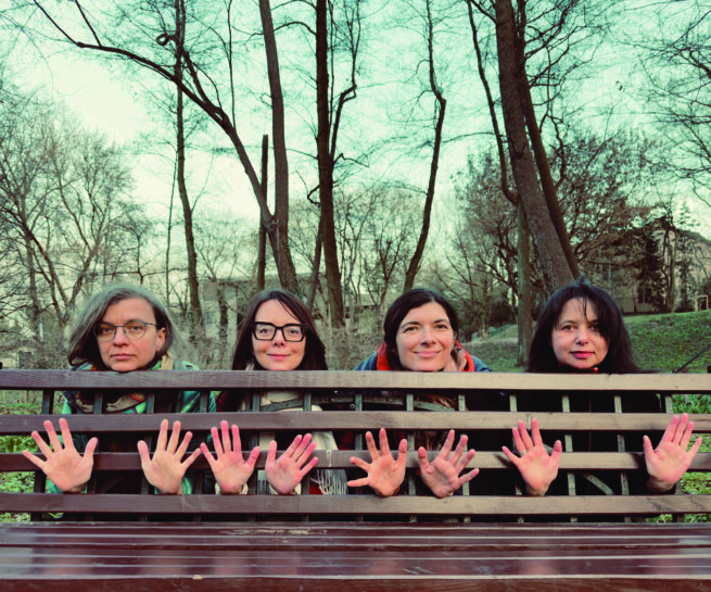 four people showing their hands from between a wooden bench