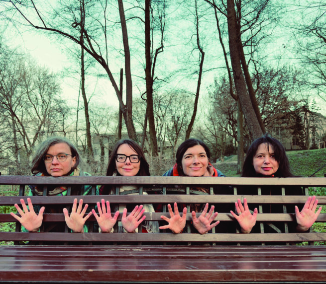 four people showing their hands from between a wooden bench