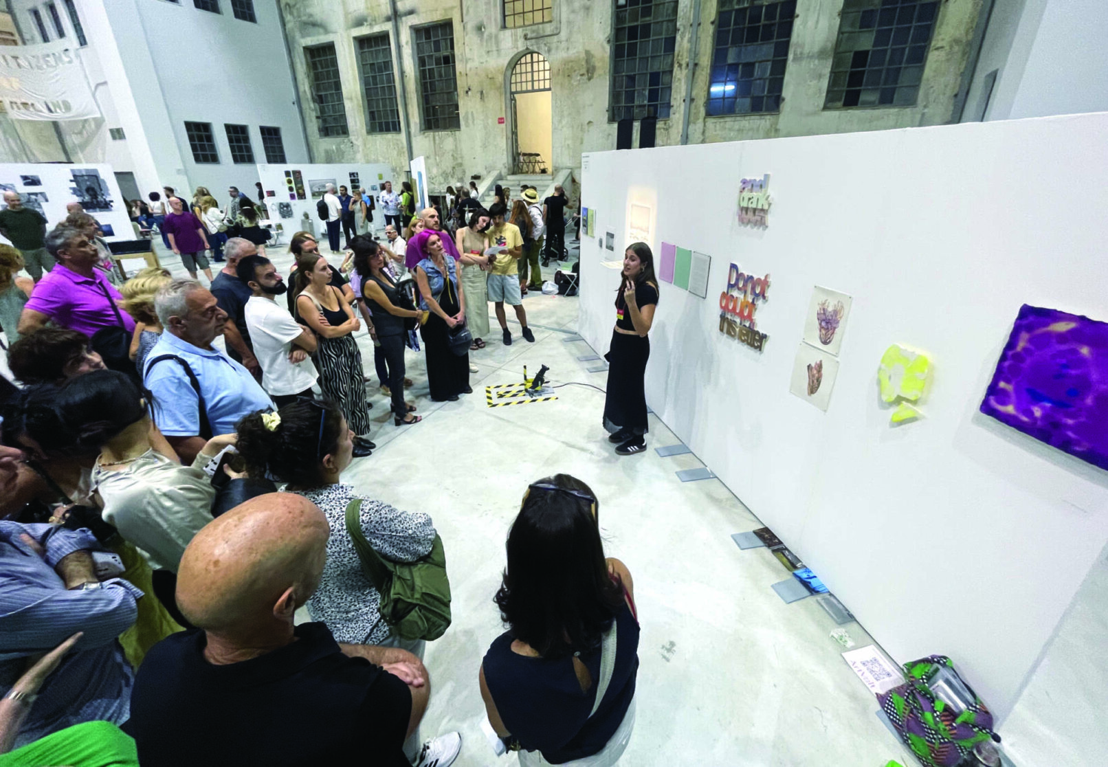 Many people are listening an artist speaking to them in front of their work