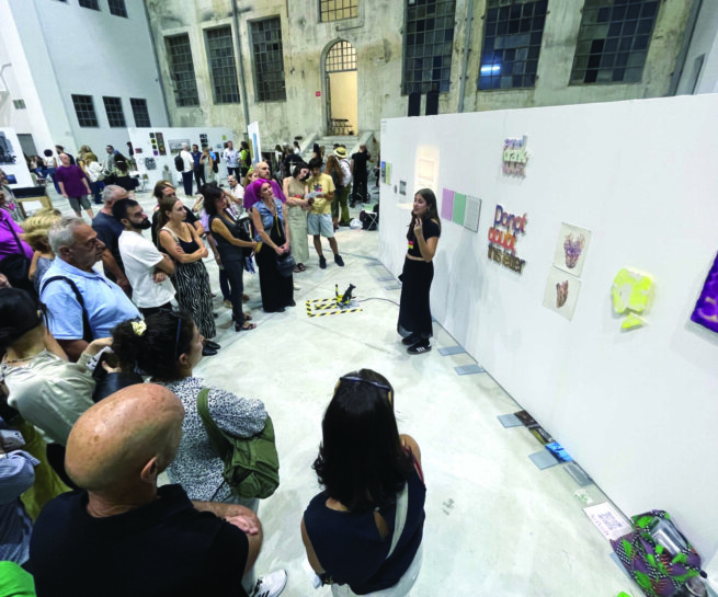 Many people are listening an artist speaking to them in front of their work