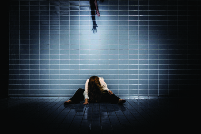 a woman sitting in front of a tiled wall