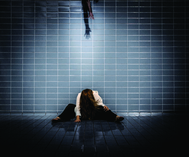 a woman sitting in front of a tiled wall